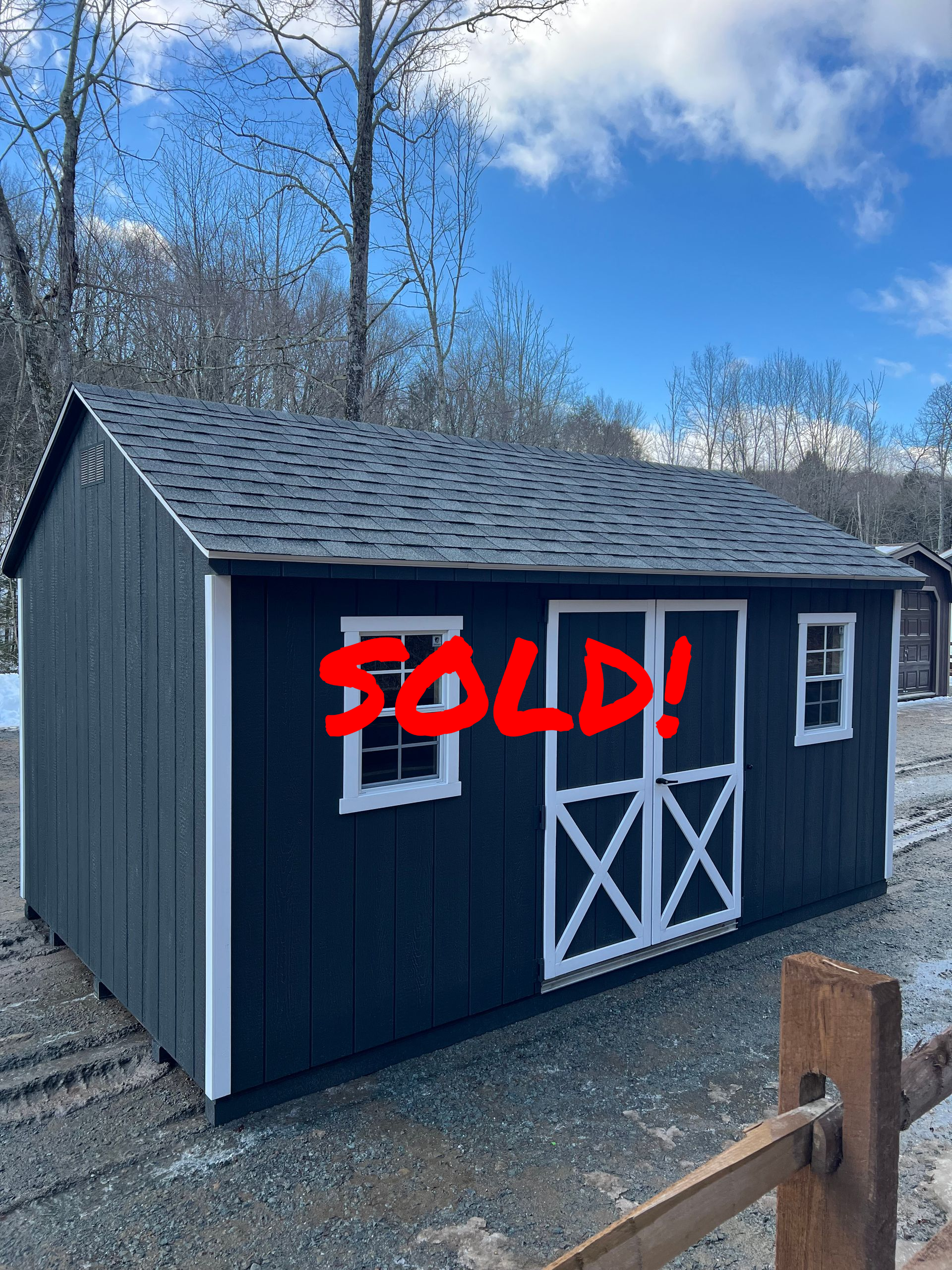 A black shed with a white door and windows is sitting next to a wooden fence.