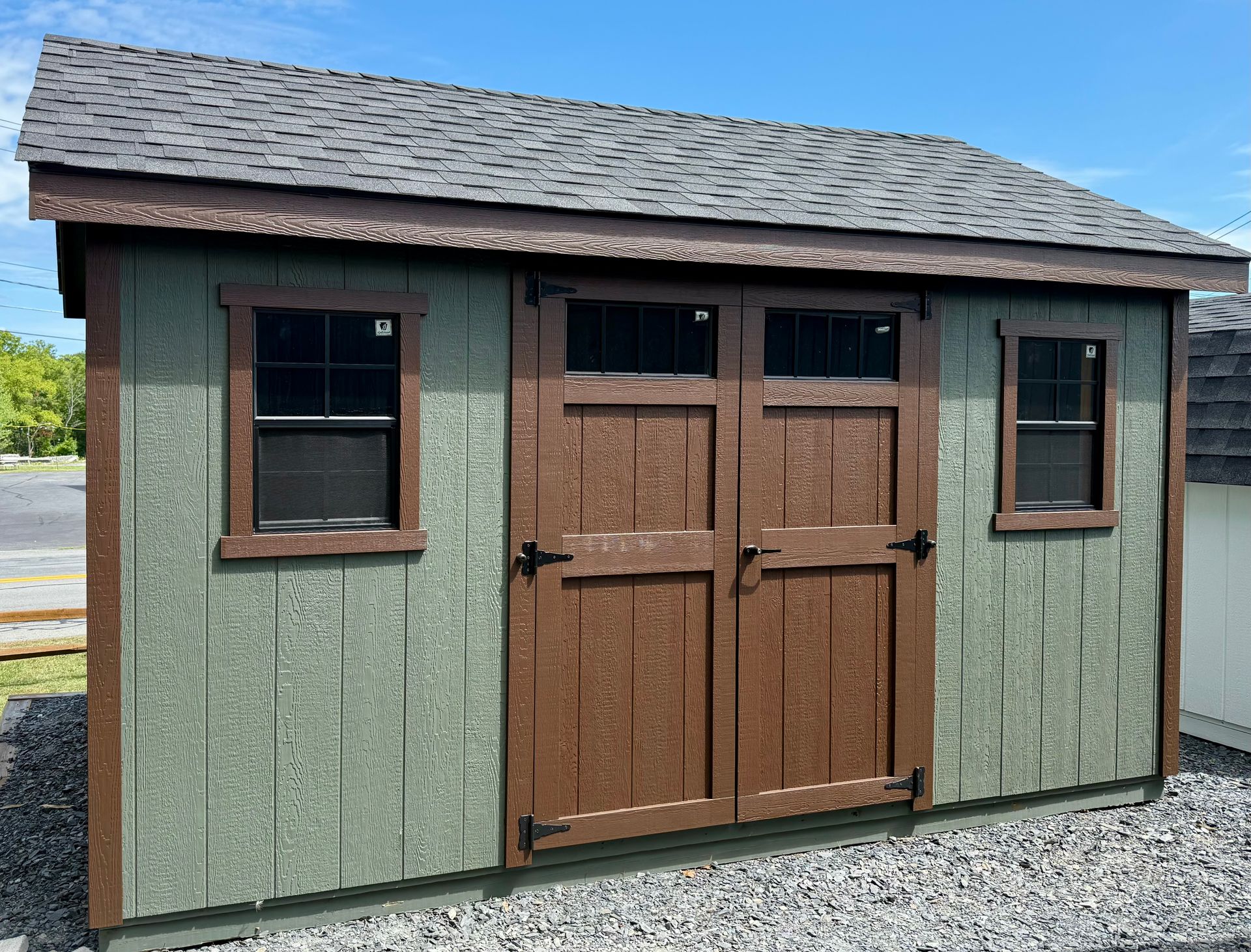 A green shed with a roof and two windows is sitting on top of a gravel lot.