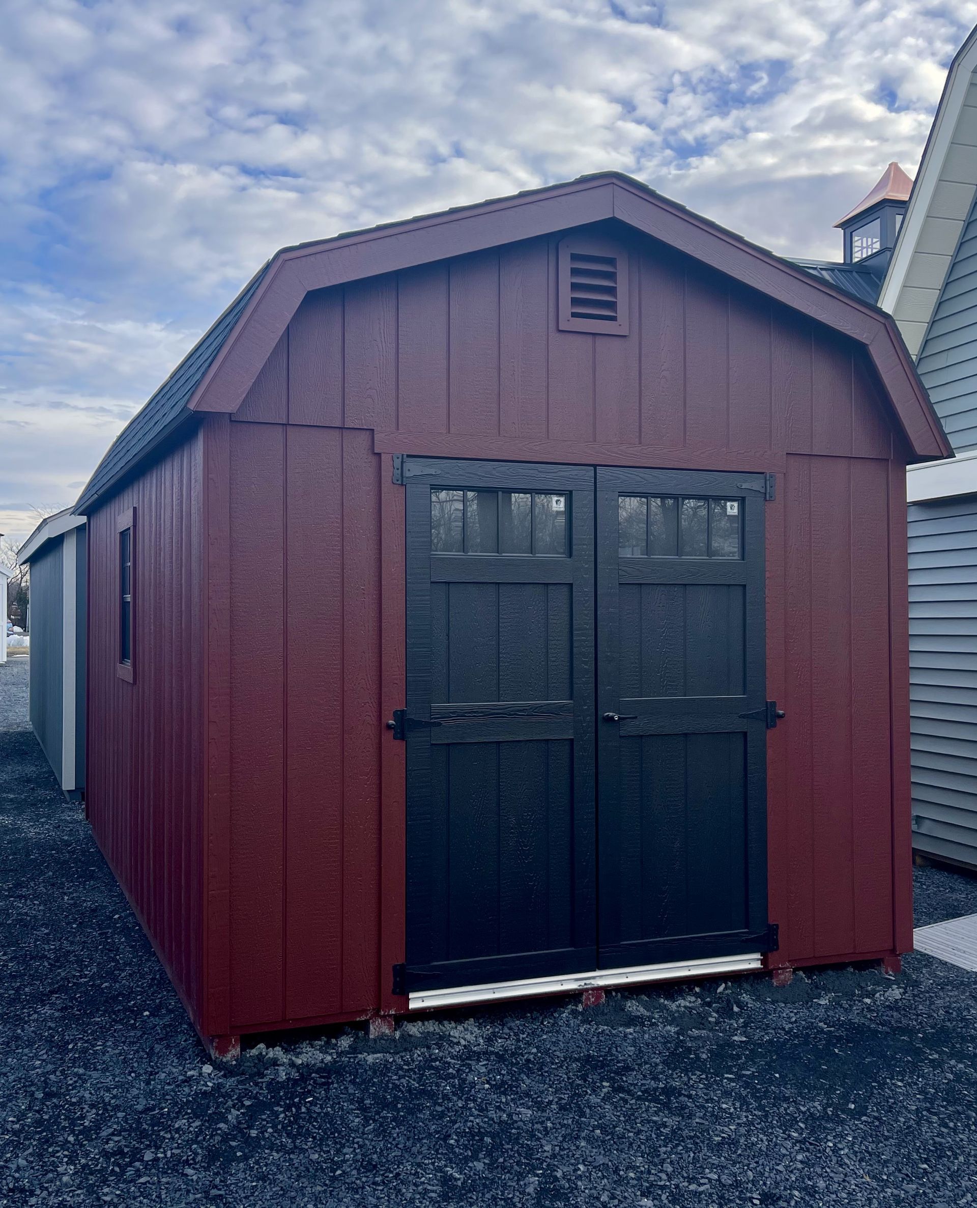 A red barn with black doors is sitting on top of a gravel lot.