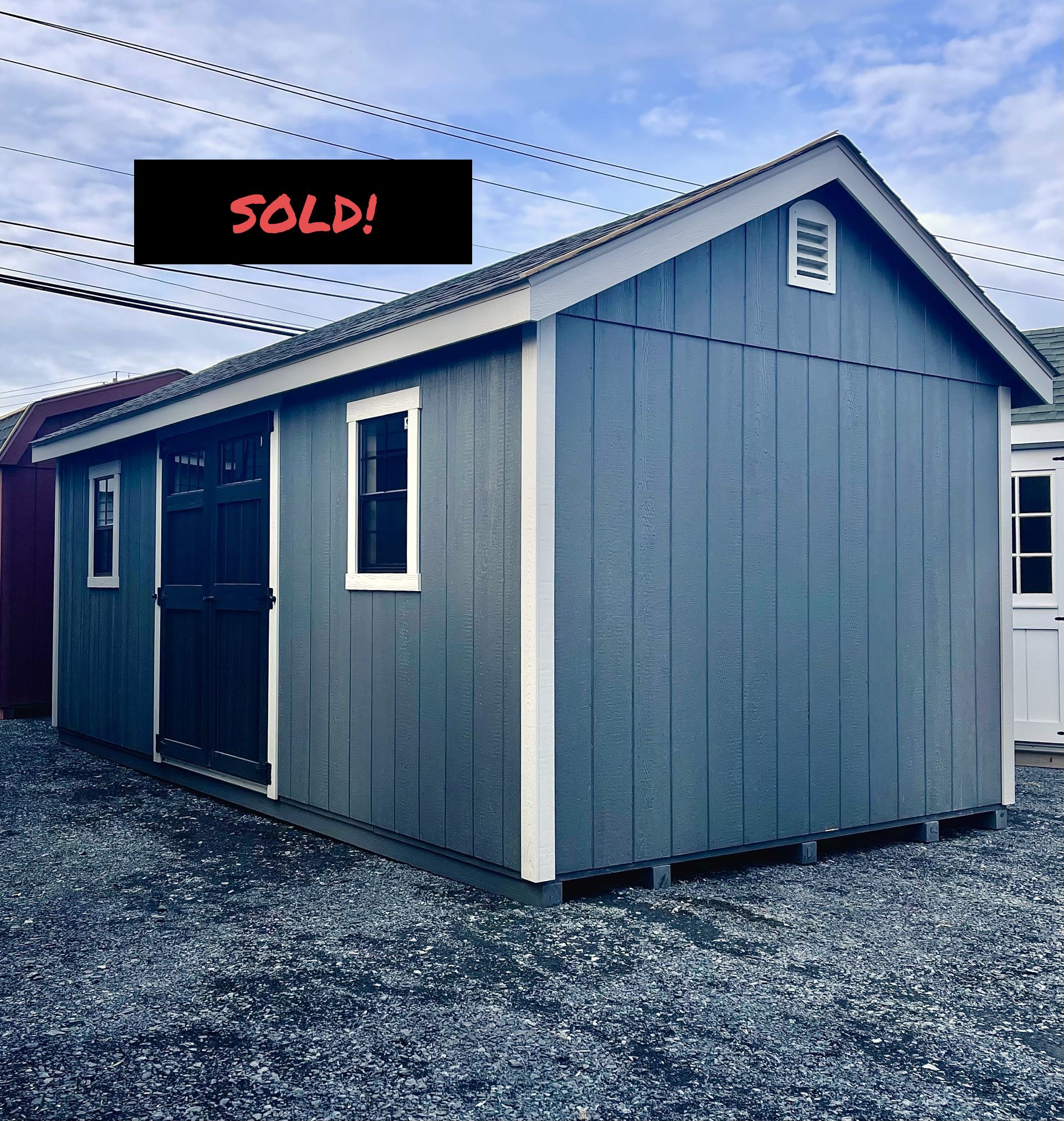 A blue shed with a white trim sits in a gravel lot