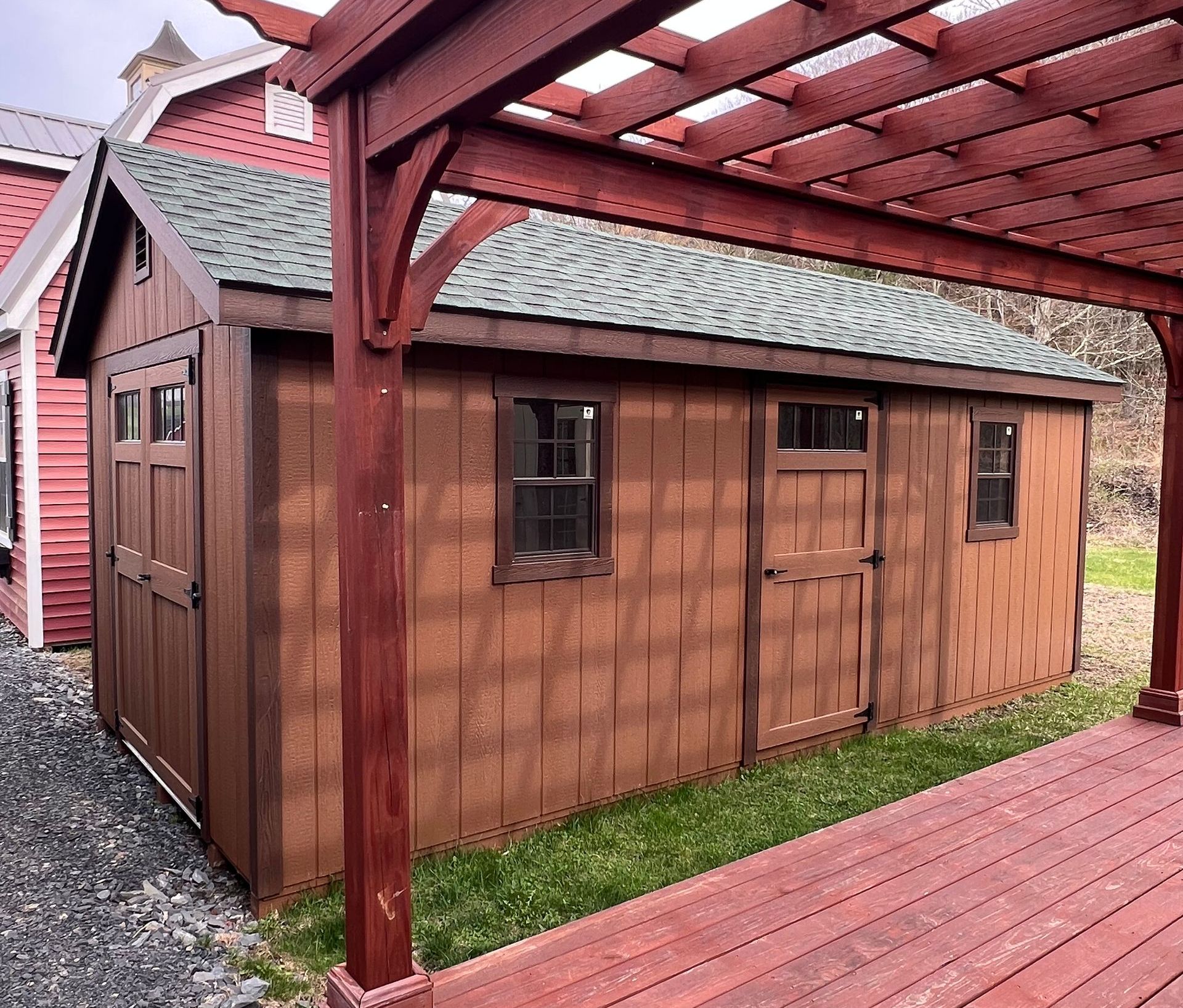 A brown shed with a green roof is under a pergola