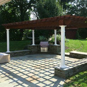 A patio with a pergola and a grill underneath it.