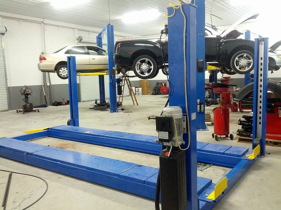 Blue car lift in a garage holding two vehicles. A white car and black pickup truck are raised.