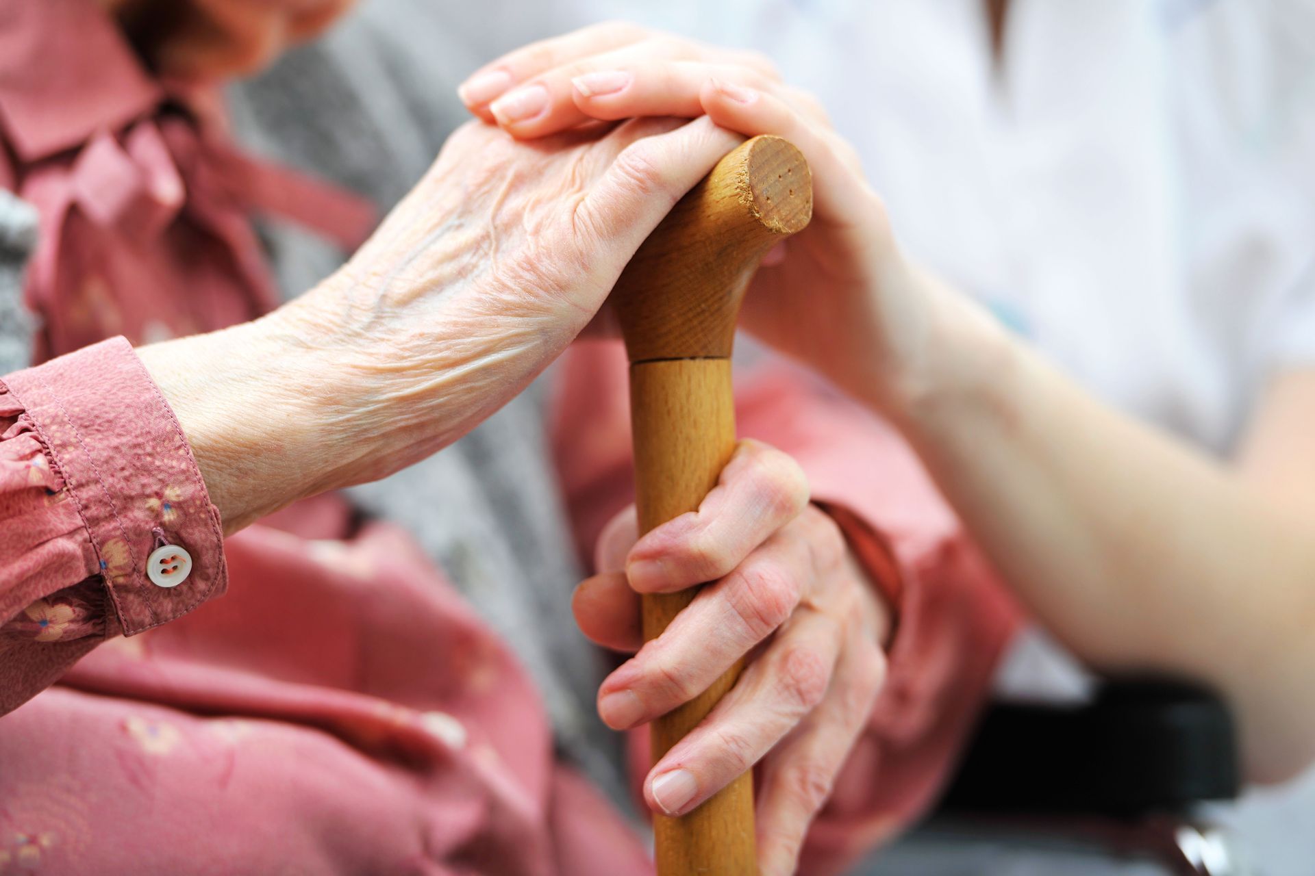 Hands of a caregiver and older person holding a cane in a close-up support scene
