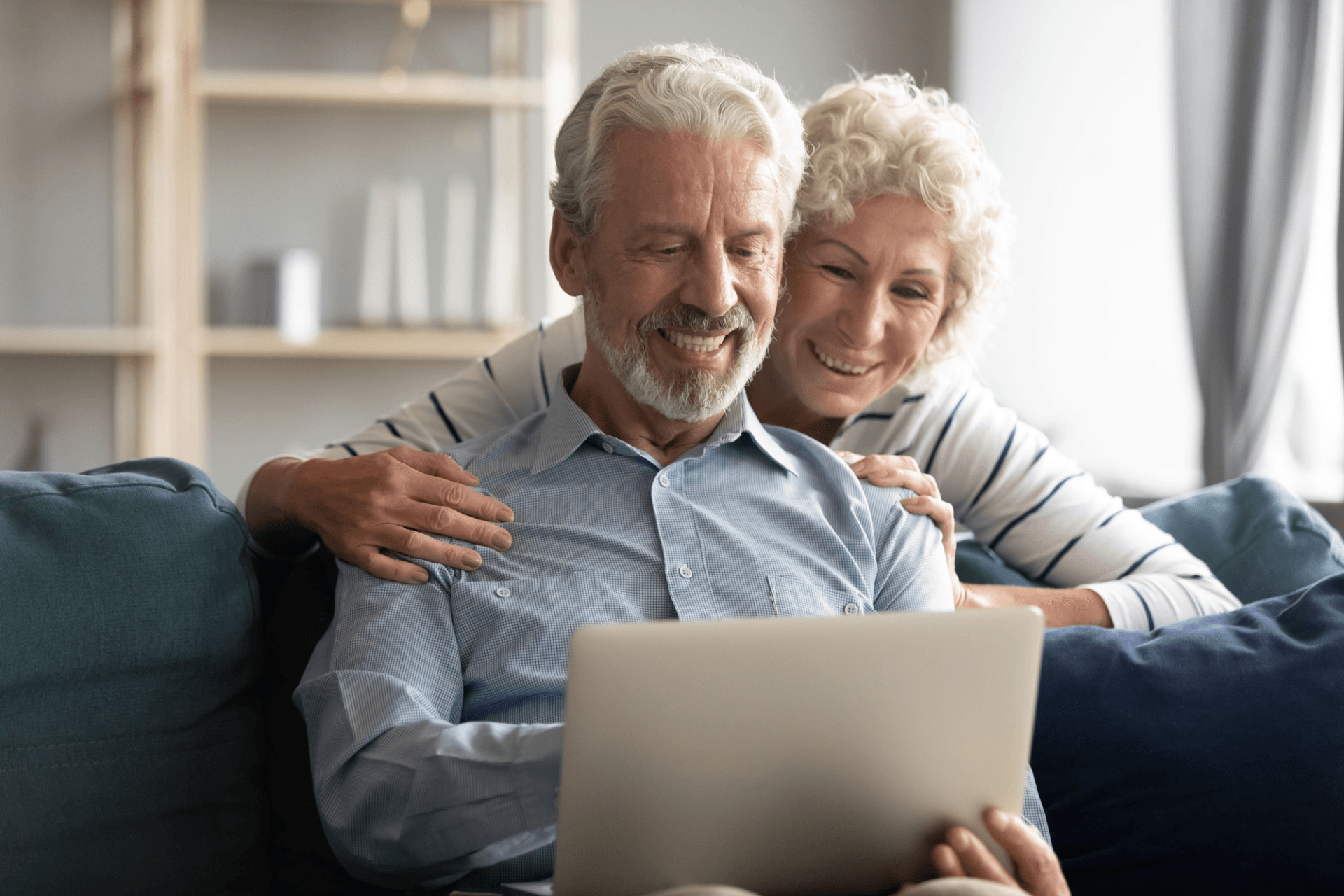 Smiling couple on a couch looking at a laptop in a bright living room