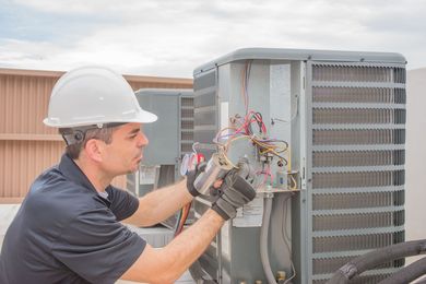 Technician in hard hat repairing rooftop HVAC unit with exposed wiring
