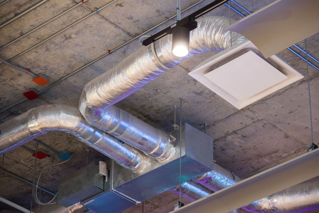 Ceiling with silver HVAC ducts, concrete panels, and a lit square vent