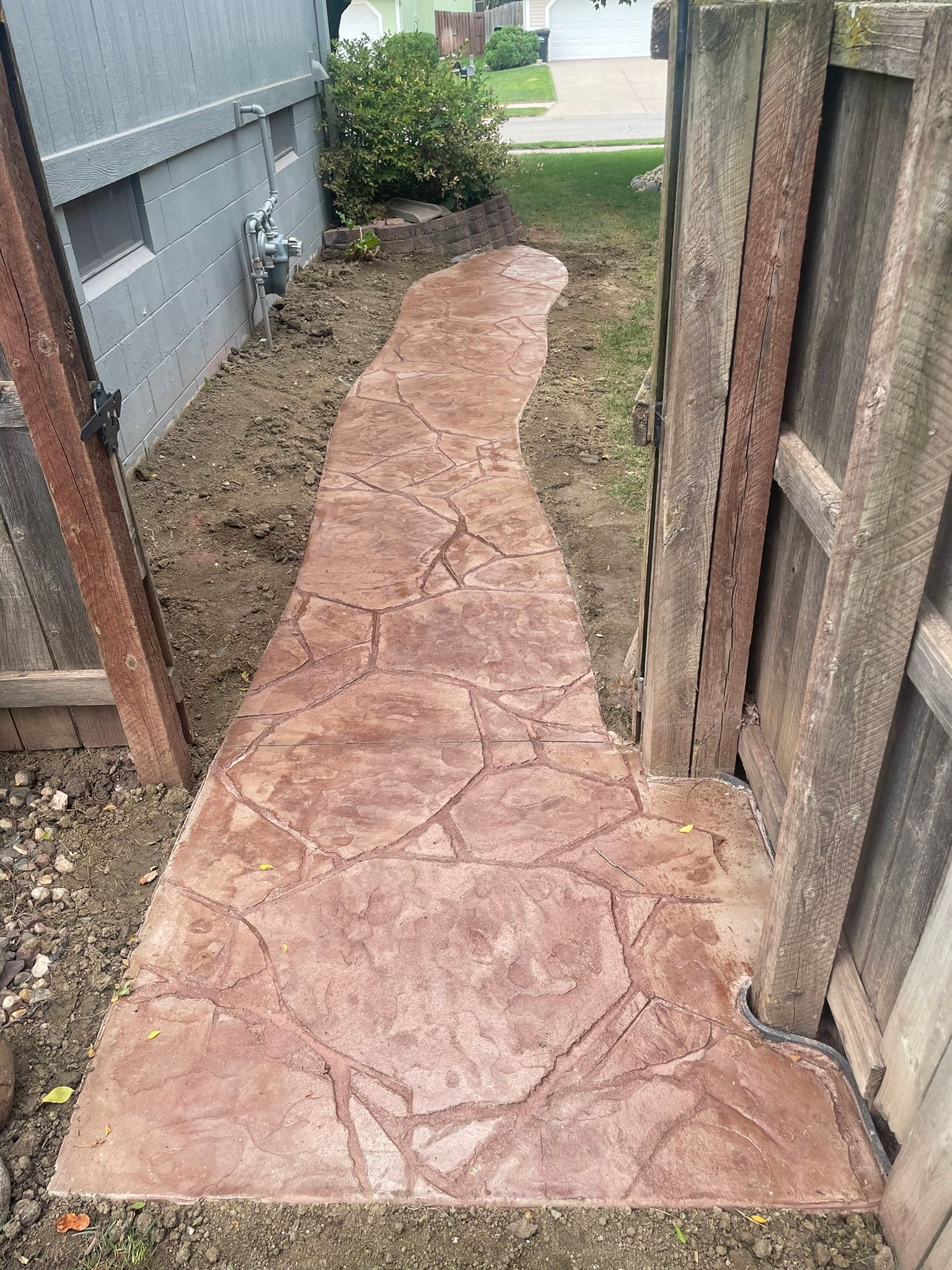 A concrete walkway leading to a fence next to a house.