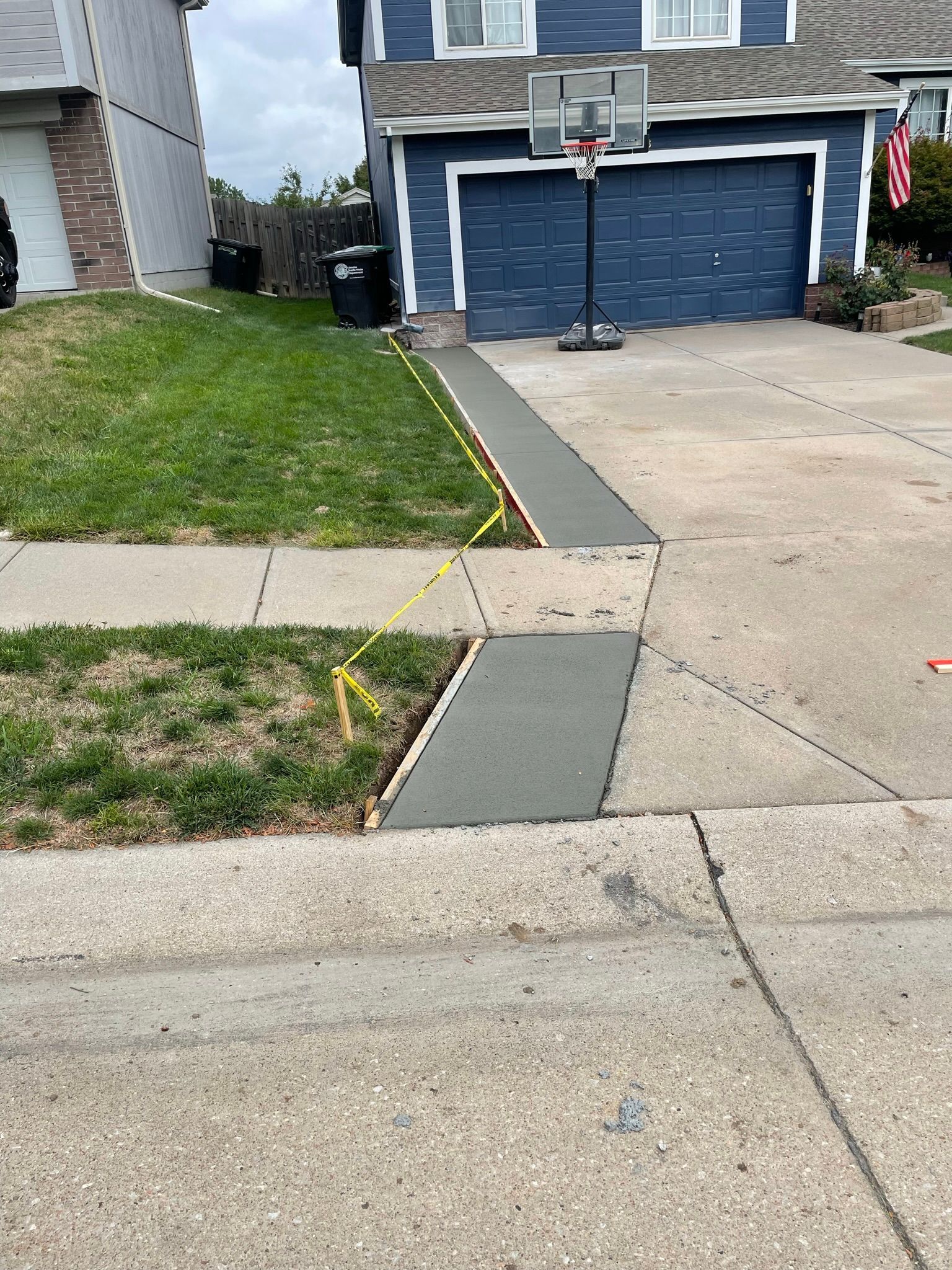 A basketball hoop is sitting on the sidewalk in front of a house.