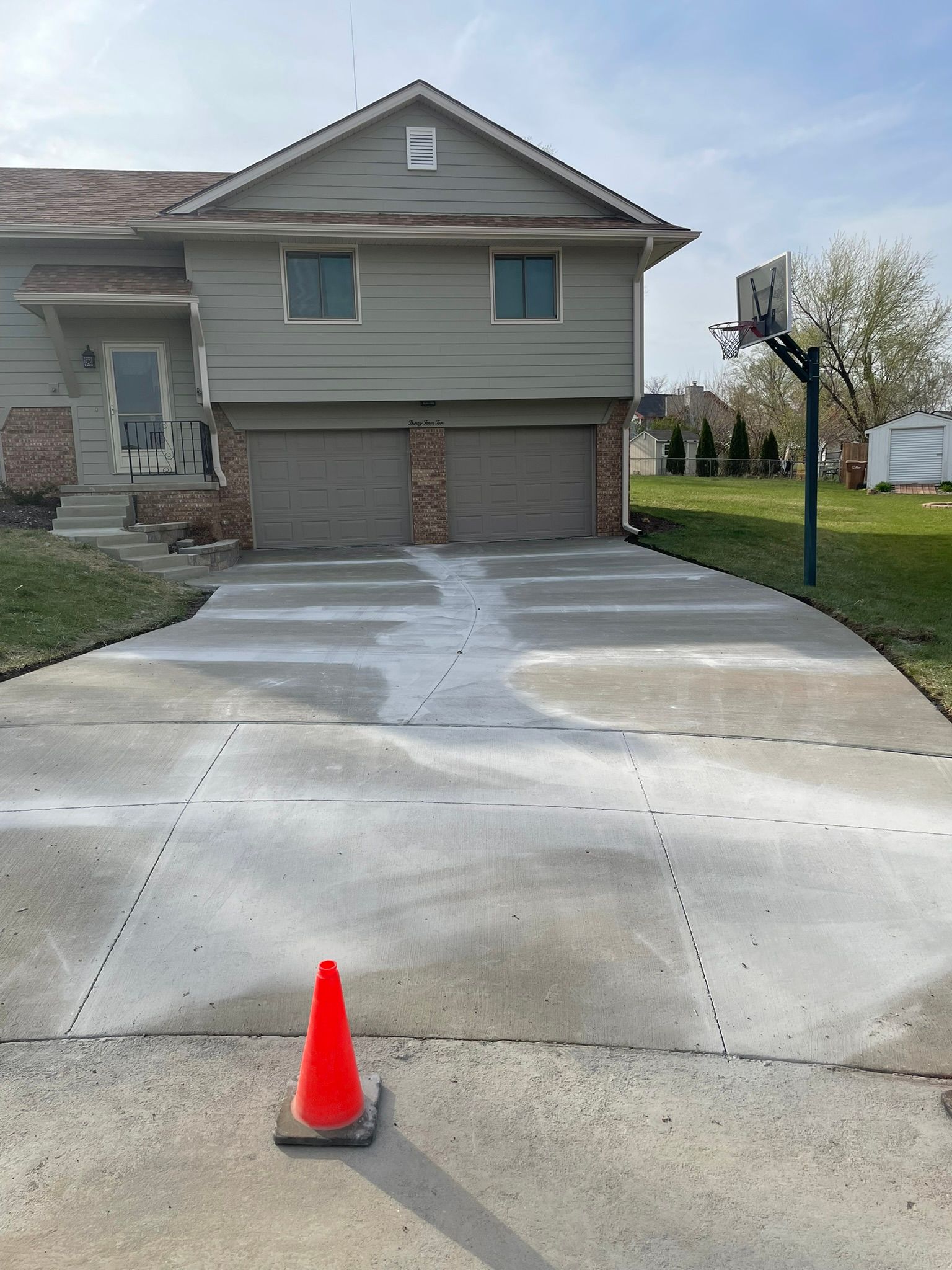 A concrete driveway with an orange cone in front of a house.