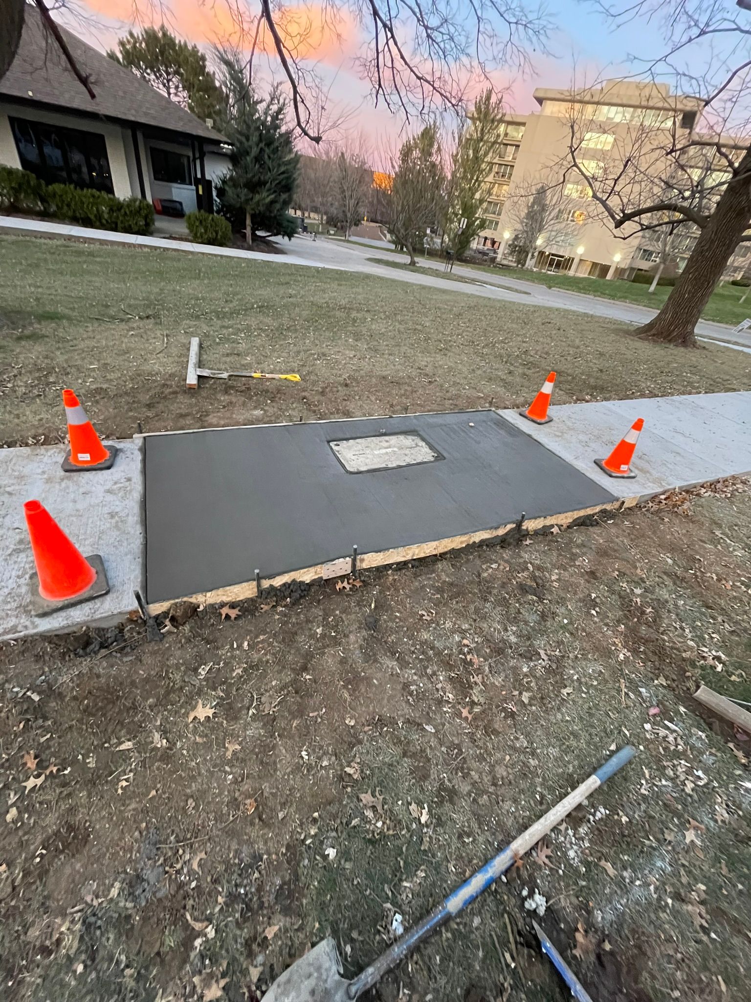 A concrete walkway is being built in a yard with orange cones and a shovel.