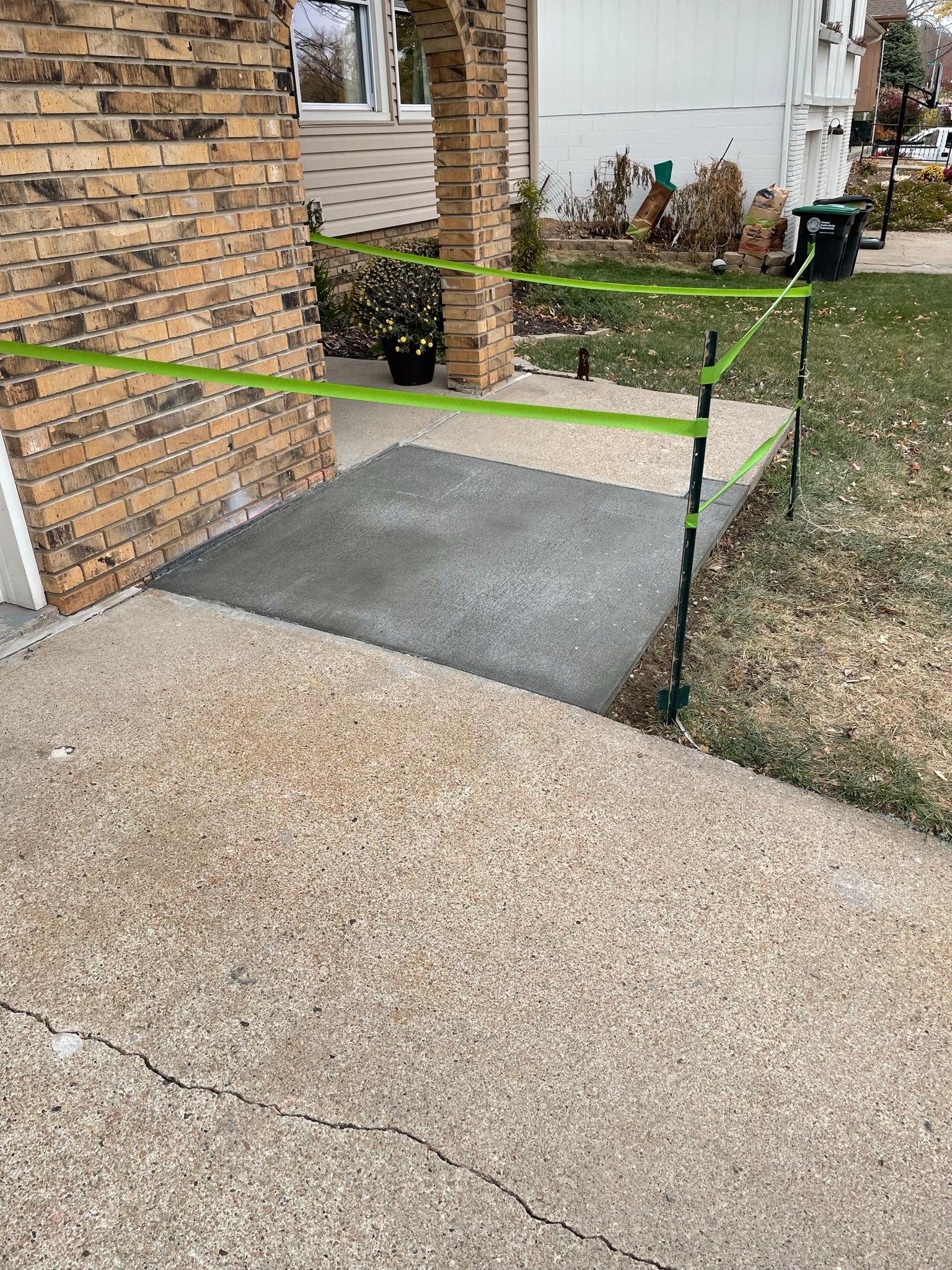 A green tape is covering a concrete walkway in front of a brick house.