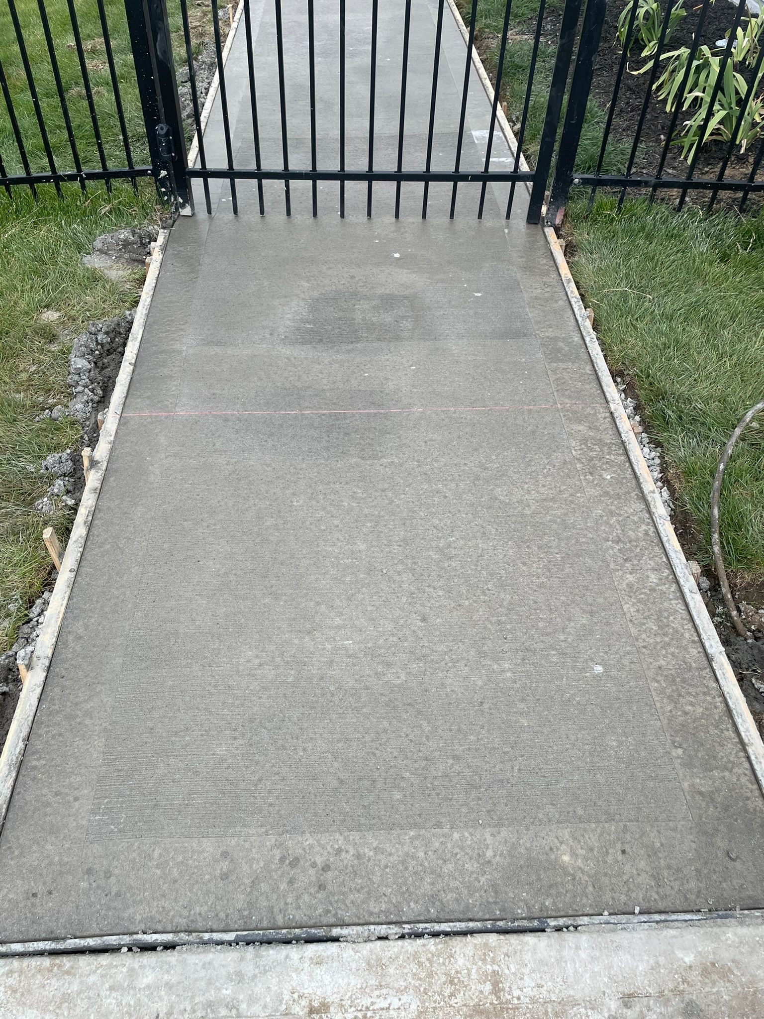 A concrete walkway with a black fence in the background.