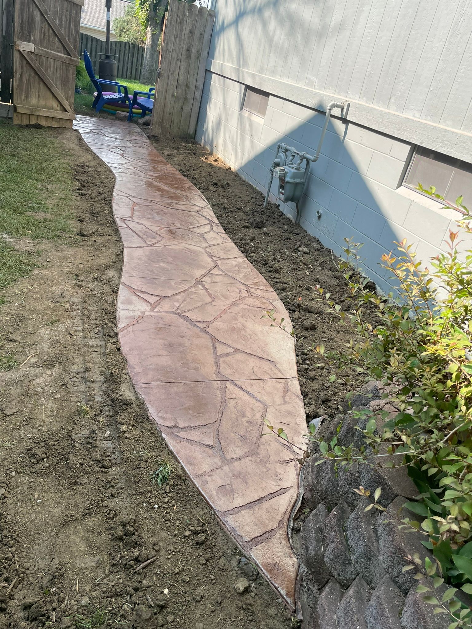 A concrete walkway leading to a house in a backyard.
