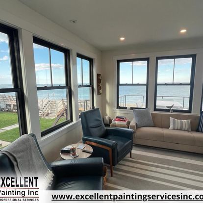A living room with a couch, chairs, and windows overlooking the ocean.