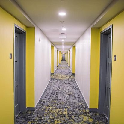 A long hallway in a hotel with yellow walls and gray doors.