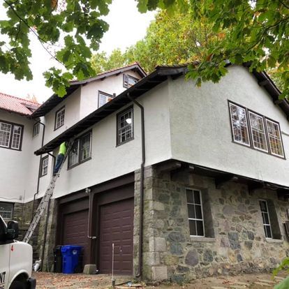 A man is painting the side of a house with a ladder.