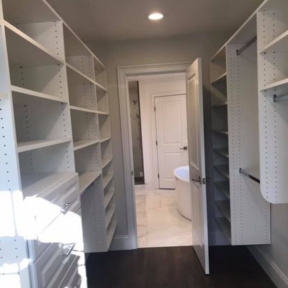 A walk in closet with lots of shelves and drawers leading to a bathroom.