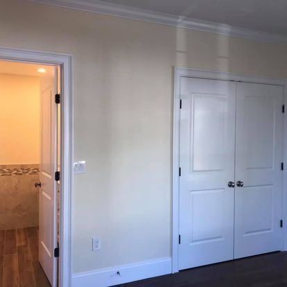 A bedroom with white walls and white doors leading to a bathroom.