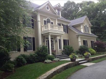 A large house with a balcony is surrounded by trees and bushes.