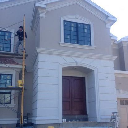 A man is standing on a scaffolding on the side of a house.