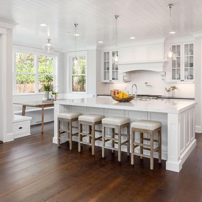 A kitchen with a large island and stools and a bowl of fruit on the counter.