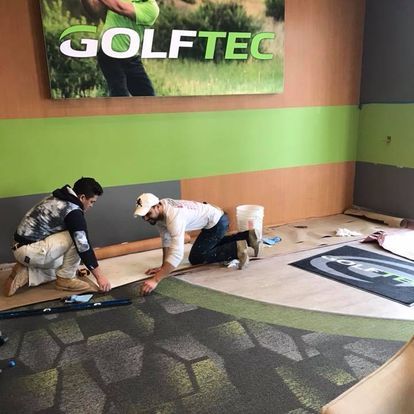 Two men are installing a carpet in a room.