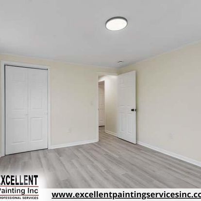 A bedroom with hardwood floors, white walls, and a ceiling light.