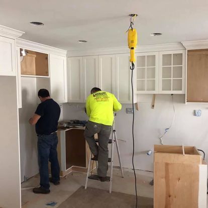 A man in a neon yellow shirt is standing on a ladder in a kitchen.