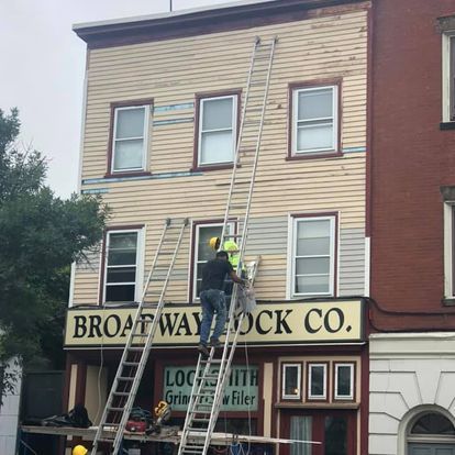 A man on a ladder is painting the side of a building that says broadway lock co.