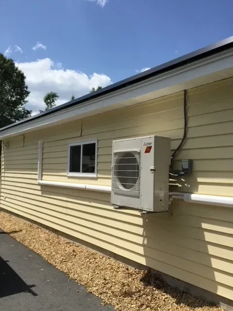 Exterior of beige house with mounted air conditioner unit beside a window under a blue sky