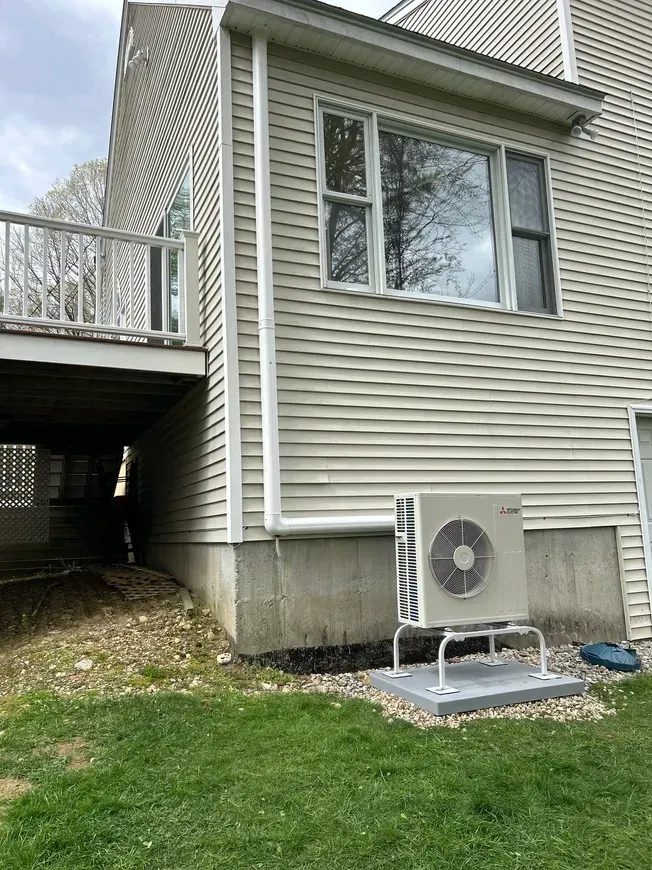 Side view of a house with a deck, windows, and a ground-mounted air conditioning unit.