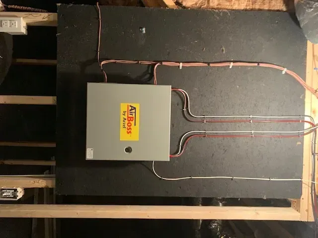 Electrical breaker panel with copper wiring mounted on a black wall in an unfinished room