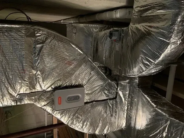 Insulated HVAC ductwork with silver foil wrapping and a small gray sensor mounted on the pipe