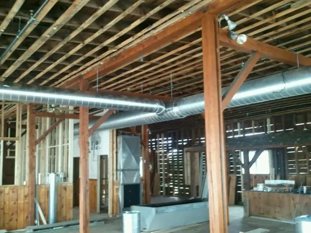 Unfinished barn interior with exposed wooden beams, metal ducting, and scattered construction materials