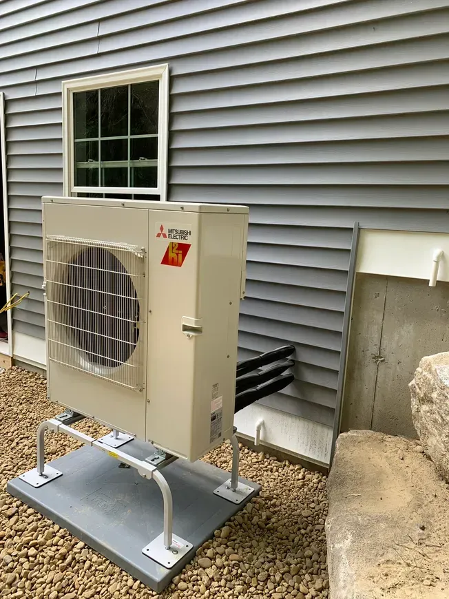 Outdoor Mitsubishi mini-split condenser unit on a platform beside a house siding wall.
