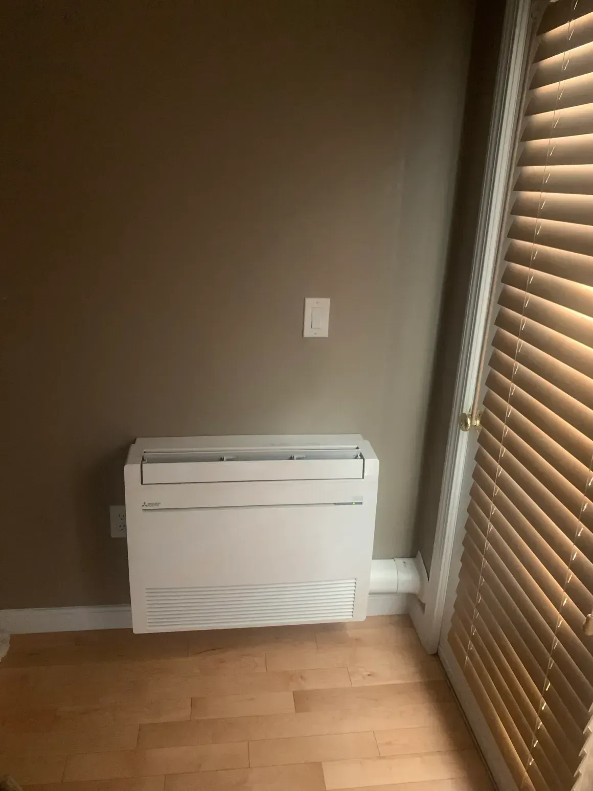 Small room corner with a white wall heater, brown walls, wood floor, and window blinds.