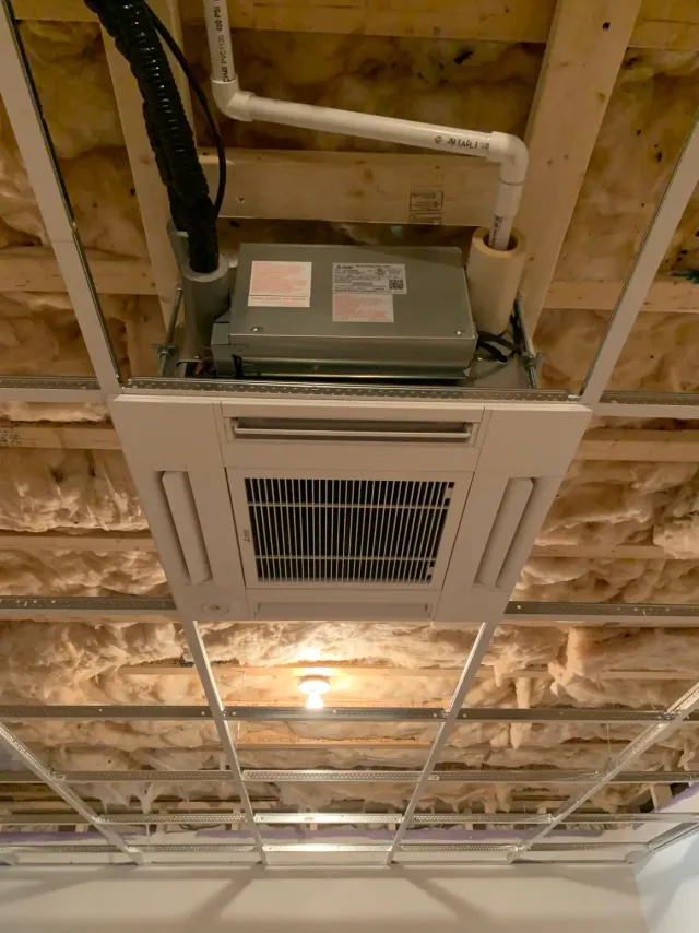 Ceiling-mounted HVAC unit in an unfinished room with exposed beams and insulation.