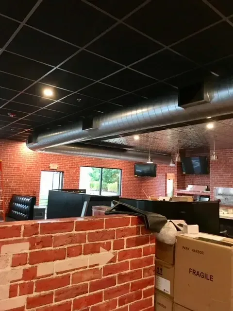 Red brick interior with black ceiling tiles, ductwork, booths, and a cardboard box in a restaurant-like space