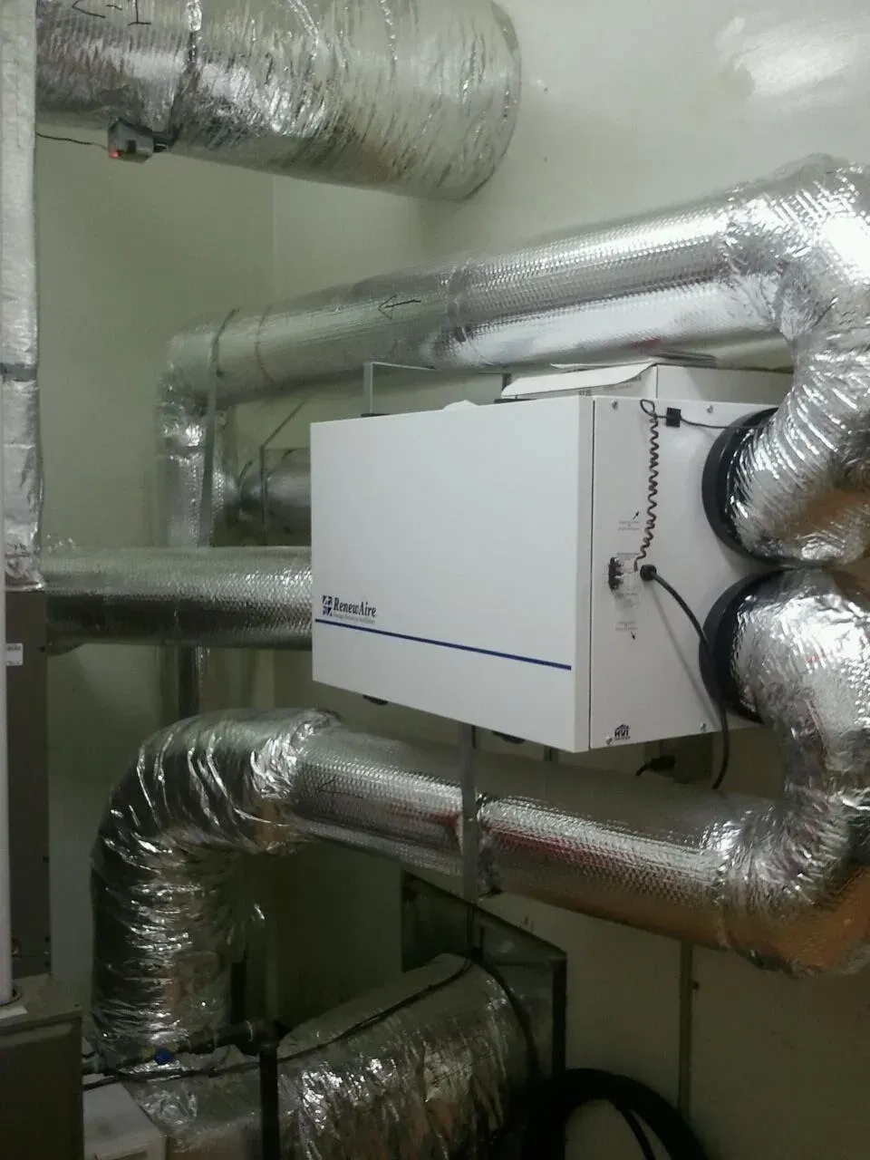 White HVAC control box amid silver insulated ductwork in a utility room