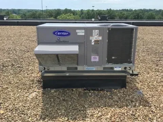 Carrier rooftop HVAC unit on a gravel rooftop with trees in the background