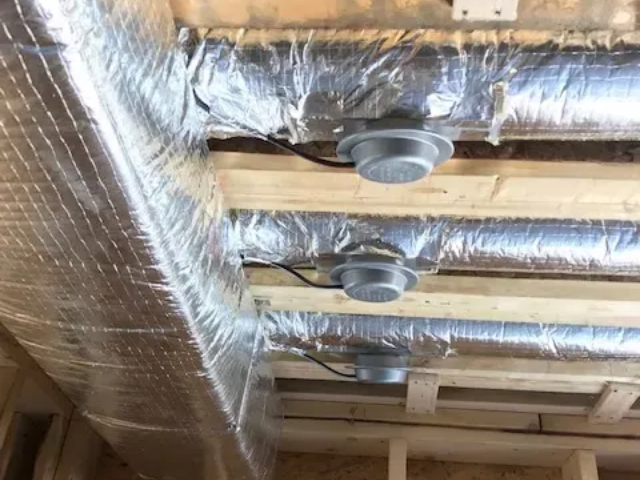Exposed ceiling with silver duct insulation and round vents in a construction space