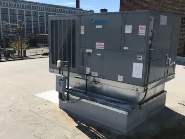 Large gray rooftop HVAC unit on a flat roof beside a building.