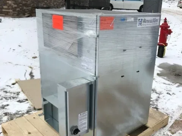 Large silver HVAC unit wrapped in plastic, sitting outdoors on snow near a red fire hydrant.