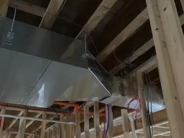 Exposed attic HVAC ductwork and metal vent installed among wooden ceiling joists under construction