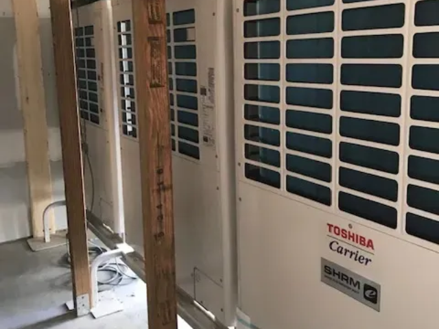 Indoor utility room with Toshiba Carrier HVAC units along a wall, partly blocked by wooden planks and debris