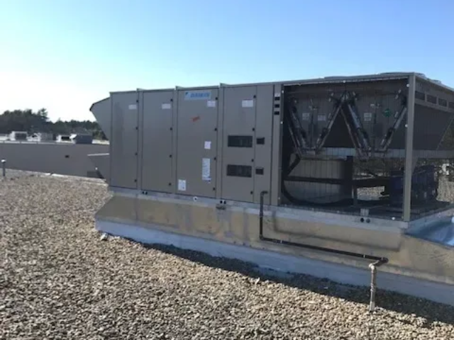 Rooftop HVAC unit on a gravel-covered building, with exposed fans and ductwork.