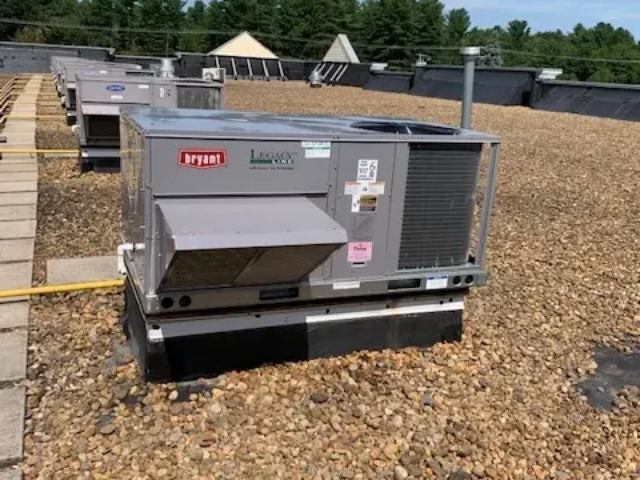 Gray rooftop HVAC unit on a gravel-covered roof with vents and warning labels.
