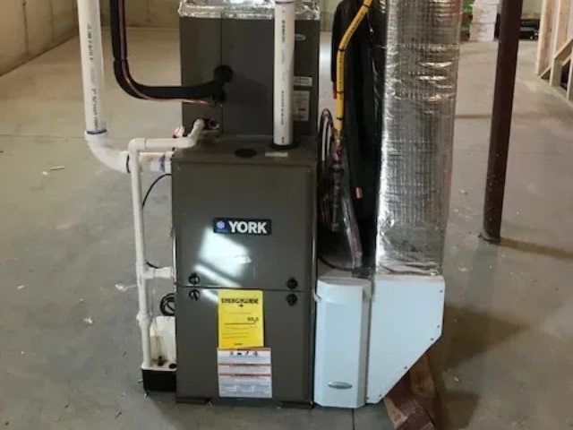 York furnace and HVAC unit in a utility room, with exposed pipes and ductwork.