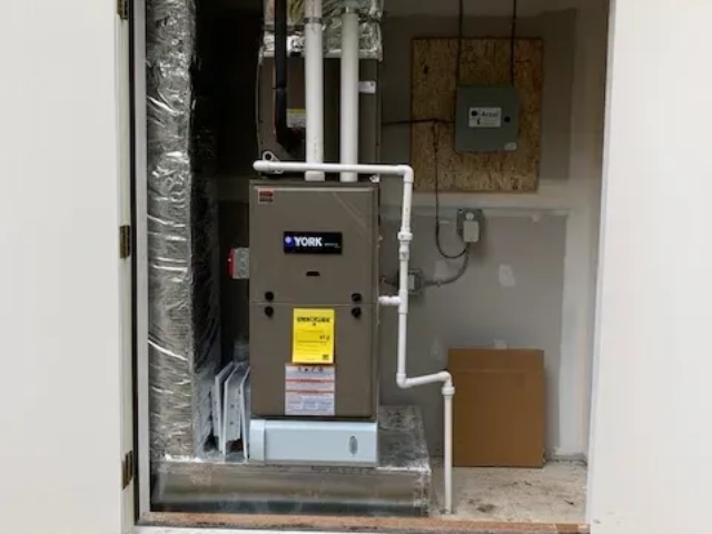 Indoor utility closet with furnace, ductwork, and exposed plumbing connections